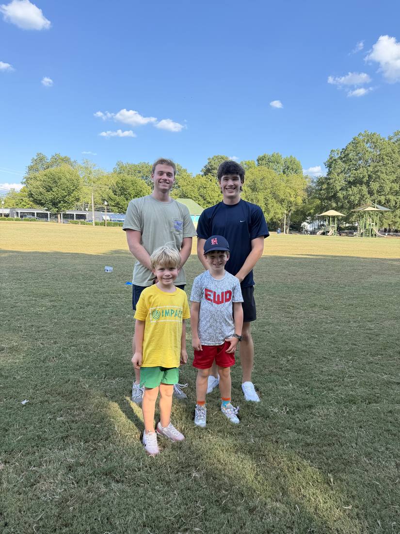 Two 55 Athletics coaches with two young athletes on the field